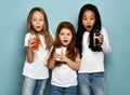 Much surprised kids girls friends in white t-shirts and blue jeans stand with glasses of water, milk and fresh juice Royalty Free Stock Photo