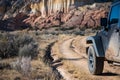 Muddy four-wheel drive vehicle on curving dirt road driving towards colorful cliffs in a high desert landscape Royalty Free Stock Photo