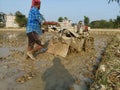 A muddy land and a farmer with his power tiller or hand tractor cultivating his own land