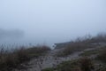 Muddy path leads to moored boat in fog Royalty Free Stock Photo