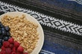 Muesli with blueberries and raspberries on tablecloth background. Granola with wild berries on towel pattern.