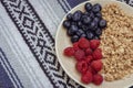 Muesli with blueberries and raspberries on tablecloth background. Granola with wild berries on towel pattern.