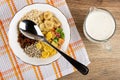 Muesli dried fruits, corn flakes, oatmeal, sunflower seeds, banana chips, spoon in bowl on napkin, jug of yogurt with cereals on