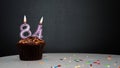 Muffin on black with a number from a candle number 84. Copy space, a pie on a black background, a card for congratulations on you Royalty Free Stock Photo