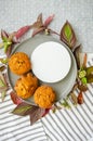 Muffins on a ceramic plate with white round podium, wooden spoon, green and red plant leaves and wild flowers on cotton tablecloth