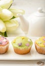 Muffins covered with icing sugar on white plate, tulips and tea pot on wooden table. Royalty Free Stock Photo