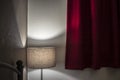 Muffled light from the floor lamp creates a relaxing, intimate atmosphere in the bedroom with thick red curtains Royalty Free Stock Photo