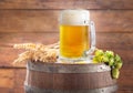 Mug of beer with wheat ears and green hops on wooden barrel Royalty Free Stock Photo