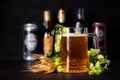 Mug of beer with wheat and hop cones against beer bottles and jars on dark wooden background. October fest background