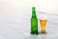 Mug and bottle of cold beer in the snow at sunset. Beautiful winter background. Outdoor recreation.