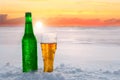 Mug and bottle of cold beer in the snow at sunset. Beautiful winter background. Outdoor recreation.