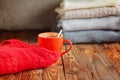 Mug with cacao or tea and red sweater on wooden table stack sweaters background.