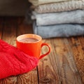 Mug with cacao or tea and red sweater on wooden table stack sweaters background.