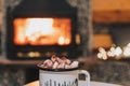 Mug of cocoa or hot chocolate with powdered marshmallows placed on a table by the fireplace