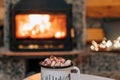 Mug of cocoa or hot chocolate with powdered marshmallows placed on a table by the fireplace