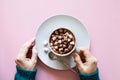 Mug with cocoa and marshmallows in female hands in knitted sweater on pink background. Top view, minimal design.