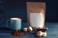 Mug of coffee, beans, paper pack, macaroons and chocolate on wooden background