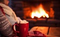 mug of coffee by the Christmas fireplace. Woman relaxes by warm fire with a cup of hot drink. Winter, Christmas holidays