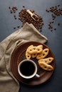 Mug of coffee and French pretzels with sugar in a brown plate on the kitchen table.