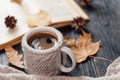 A mug of coffee in a knitted jacket, an open old book, autumn dry leaves on the table.