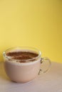 Mug of coffee with milk sprinkled with chocolate chips and foam, on yellow background. Energy and cheerfulness morning Royalty Free Stock Photo