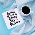 Mug of coffee on pale blue pastel chiffon cloth on a blue background. Card with handwritten inspirational quote Home is not a plac