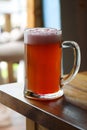 Mug of sweet cold light beer with pomegranate juice and foam on the restaurant table. Real life photography at a restaurant, sunny Royalty Free Stock Photo