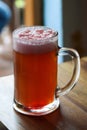 Mug of sweet cold light beer with pomegranate juice and foam on the restaurant table. Real life photography at a restaurant, sunny Royalty Free Stock Photo