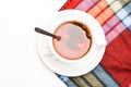 Mug filled with hot black brewed tea and spoon on colorful cozy plaid background. Tea mug with dipped bag of tea on