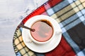 Mug filled with hot black brewed tea and spoon on colorful cozy plaid background. Tea mug with dipped bag of tea on