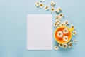 A mug of flowered chamomile tea and a blank empty sheet of white paper on a blue background with spread out flowers.