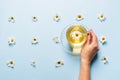 A mug of flowered chamomile tea in woman`s hand on a blue background with flowers spread out. Floral summer background.