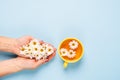 A mug of flowered chamomile tea in woman`s hand on a blue background with flowers spread out. Floral summer background.