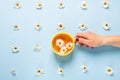 A mug of flowered chamomile tea in woman`s hand on a blue background with flowers spread out. Floral summer background.