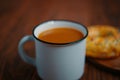 White metal mug with a drink and pastries on a wooden table.