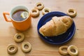 Mug full of black tea with lemon, croissant on plate and small bagels