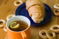 Mug full of black tea with lemon, croissant on plate and small bagels