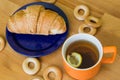 Mug full of black tea with lemon, croissant on plate and small bagels