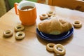 Mug full of black tea with lemon, croissant on plate and small bagels