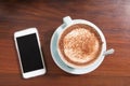 A mug of hot chocolate and smart phone on wooden table.