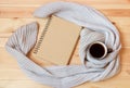 Mug of hot coffee, empty notebook and scarf on wooden background