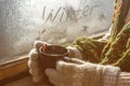 mug with hot drink coffee or tea in the hands of a girl in a sweater and mittens on the background of a frozen winter window