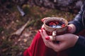Mug of hot tea in woman hand is autumn in a forest foliage. Autumn came, magical mood. Red berries floating in the tea.