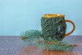 Mug in knitted cover standing next to a Christmas