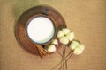 A mug of milk on a saucer with cinnamon and cotton flowers on a table covered with burlap. Top view. Pottery on the table