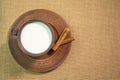 A mug of milk on a saucer with cinnamon are on a table covered with burlap. Top view. Pottery on the table