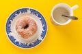 A mug with plant based milk and a plate with sugar coated doughnut, on yellow background