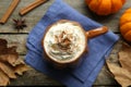 Mug of pumpkin spice latte with whipped cream, ingredients and dry leaves on wooden table, flat lay