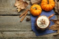 Mug of pumpkin spice latte with whipped cream, ingredients and dry leaves on wooden table, flat lay. Space for text