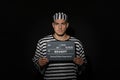 Mug shot of prisoner in striped uniform with board on black background, front view Royalty Free Stock Photo